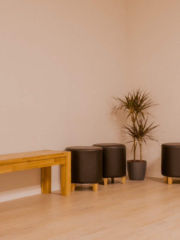 Ein minimalistisch eingerichteter Raum mit einem Holztisch, zwei runden Hockern und einer Topfpflanze.