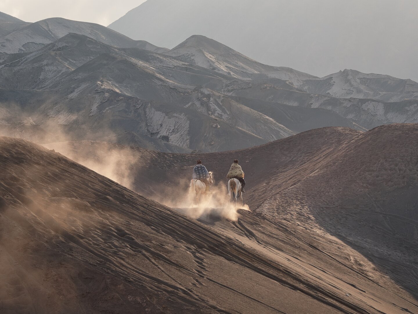 The horsemen trot away from the camera, more volcanic ridges are visible with a partially imposing mountain in the background