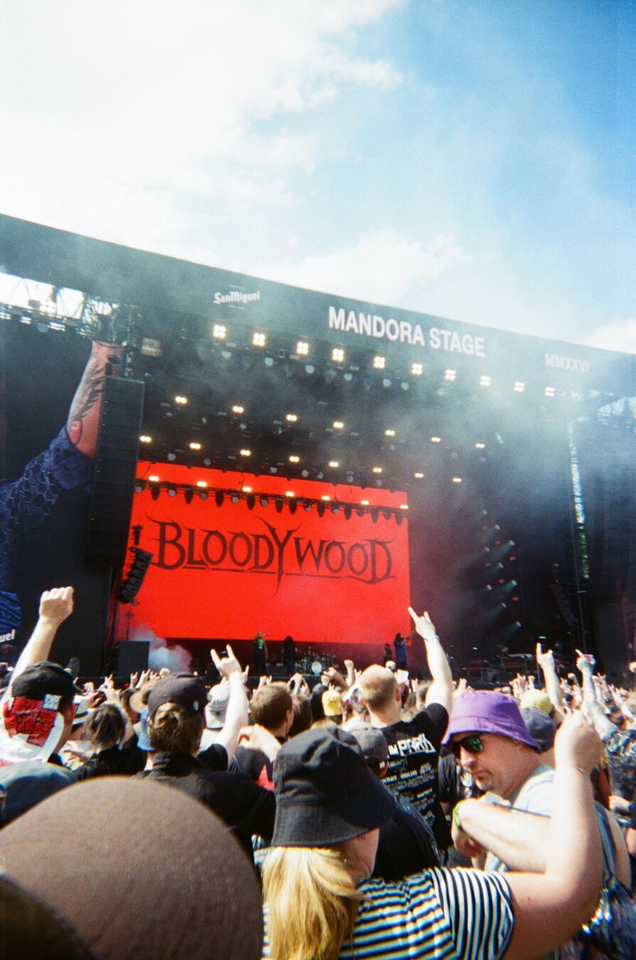 Anslog color photo of the „Mandora stage“ at Rock im Park 2026. The video screen shows black on red „Bloodywood“, the name of the indian metal band playing. Crowd shows plenty of devils horns. 🤘🤘 Pretty cool performance, damn great band. Keep on rocking, guys!