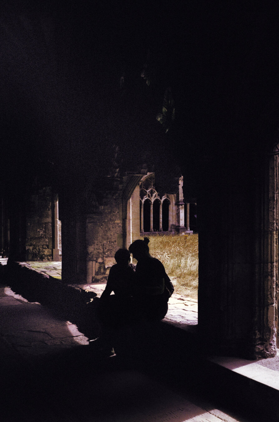 Analog color photo of the shadows of two people sitting in an arch, talking to each other. A gothic window can be seen in the background. Colors are edited, as the film used originaly gives a turquoise touch. Here the colors are close to its normal colors.