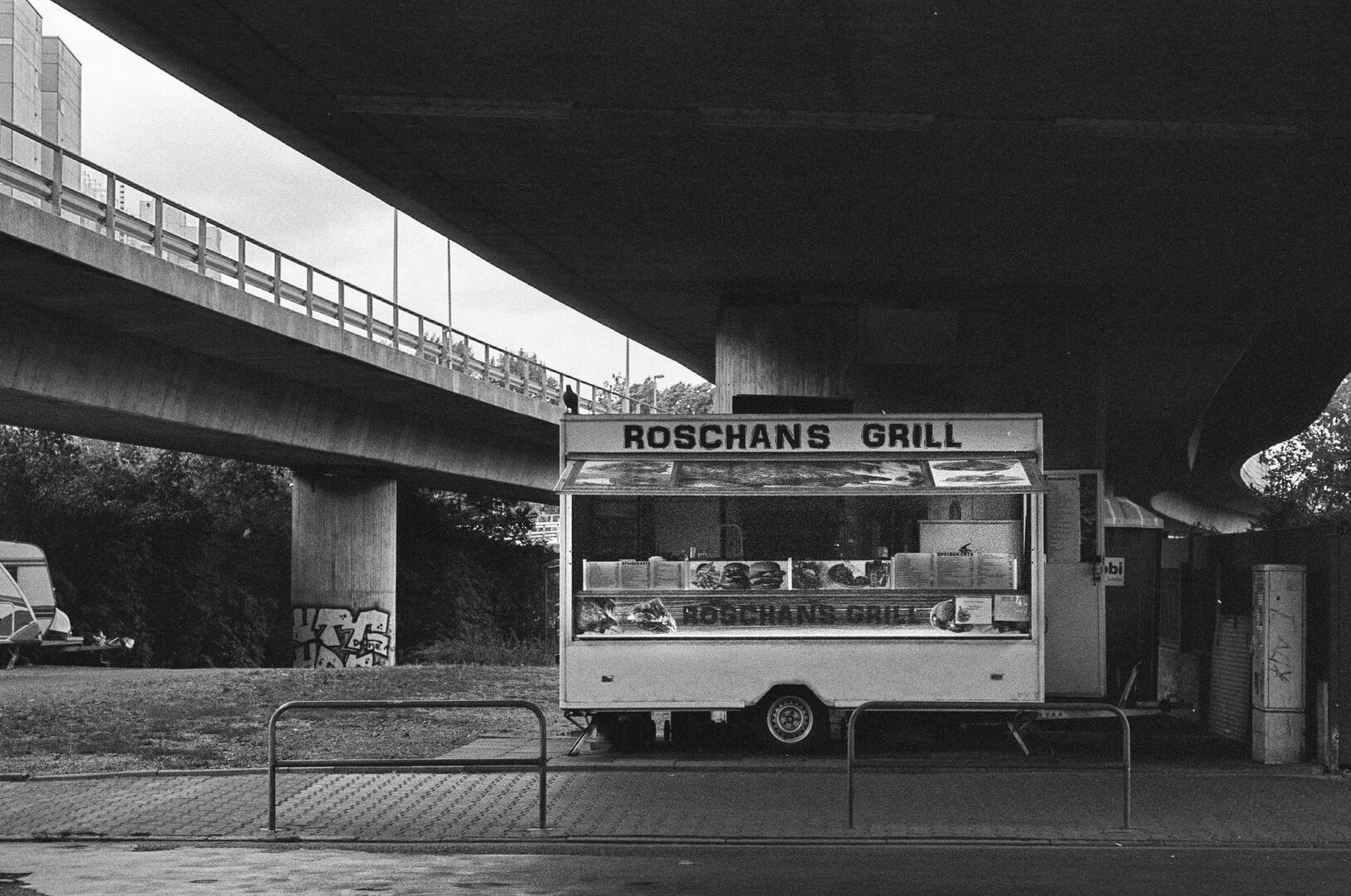 A grill stand under the bridge of Rosa-Luxemburg-Street. Its „Roschans Grill“, selling fries, burger and grilled chicken at that spot since the early 90s.