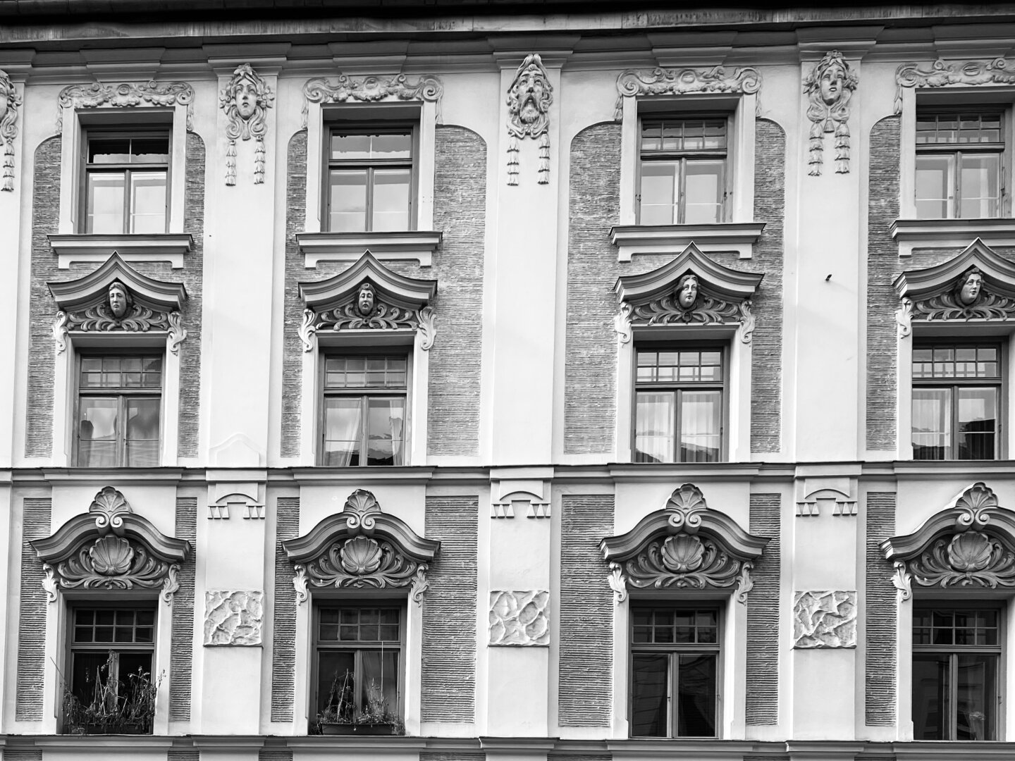 Schwarz-weiß Detailaufnahme der Jugendstil-Fassade eines Gebäudes.
Hier im Bild sieht man die typische Fassadengliederung dieser Stilepoche und vor allem die Ornamentik der Fenstergestaltung.
Fotografiert in der Münchner Innenstadt. 

A black-and-white close-up of a building's Art Nouveau façade.
The image shows the characteristic façade layout of this stylistic era and, above all, the ornamentation of the window design.
Photographed in Munich's city center.