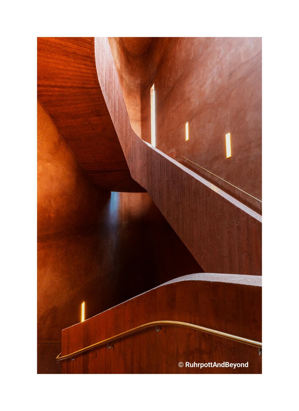 Blick in ein Treppenhaus aus Sichtbeton. Farbe terracotta. Warm, harmonisch geschwungen.
