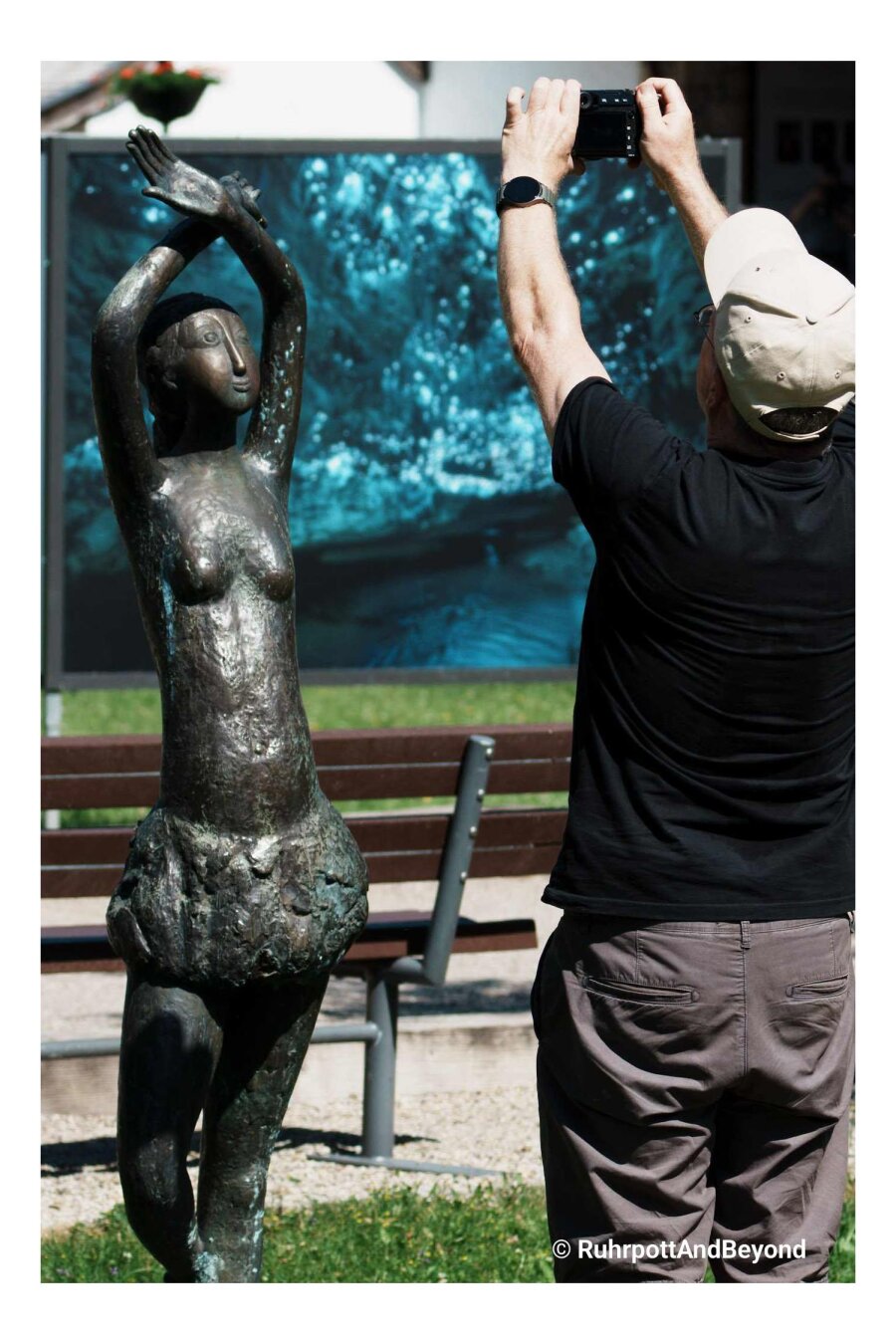 Ein Fotograf der sie Skulptur einer Frau fotografiert, nimmt die gleiche Haltung ein wie die Skulptur