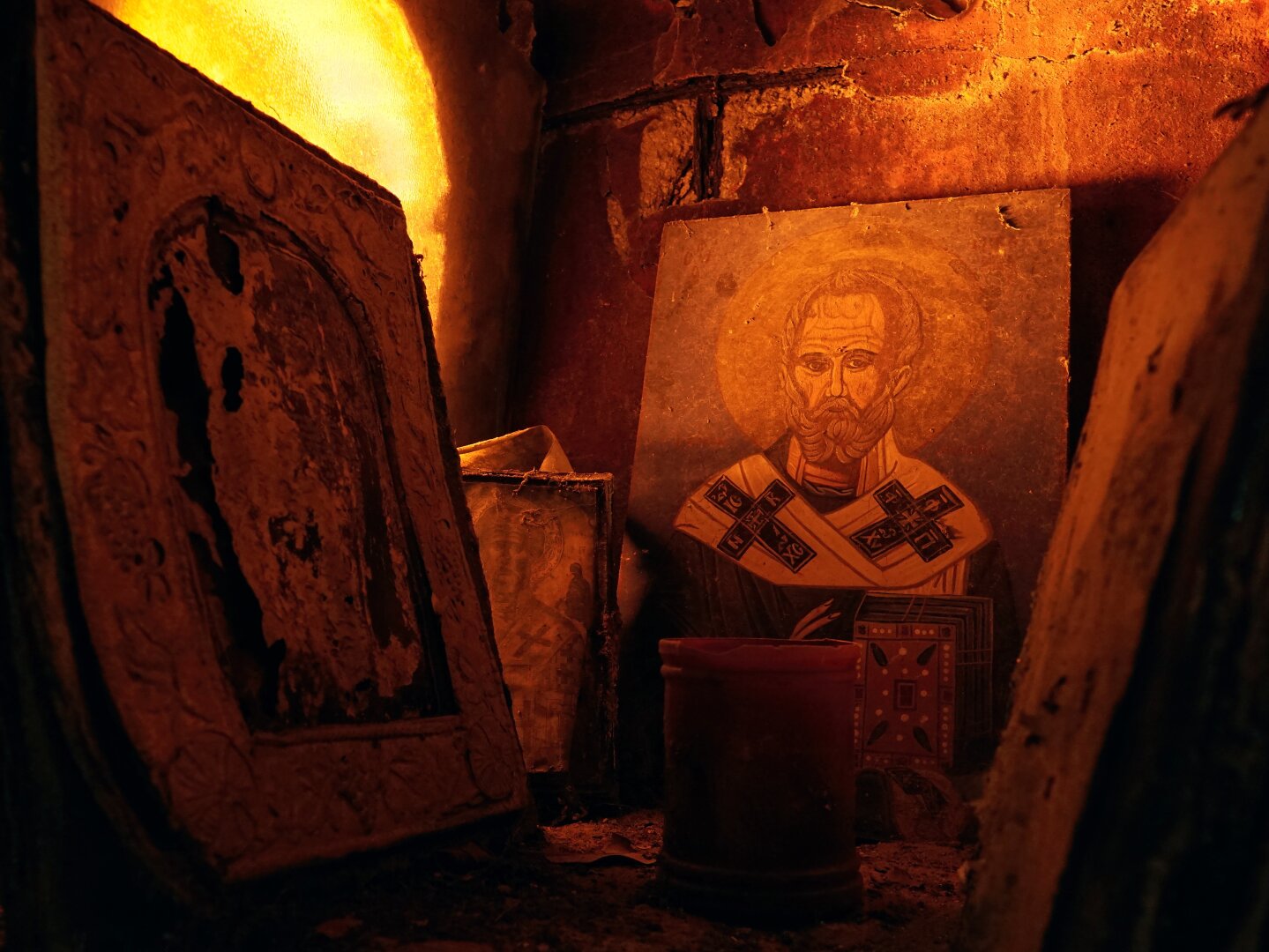 A shrine at night. The lighting is orange. Two books are framing a drawn picture of Saint Nicholas, leaning on a rustic wall.