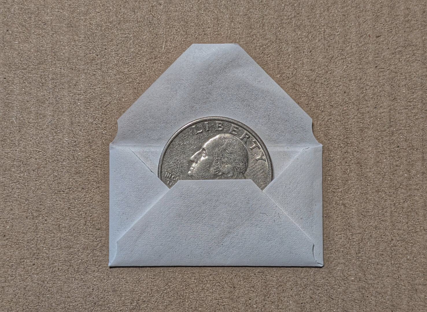 A US quarter is partly inserted into a tiny envelope just barely large enough to accommodate it. The envelope is what my razor blades come packaged in. It's all just so absurd.