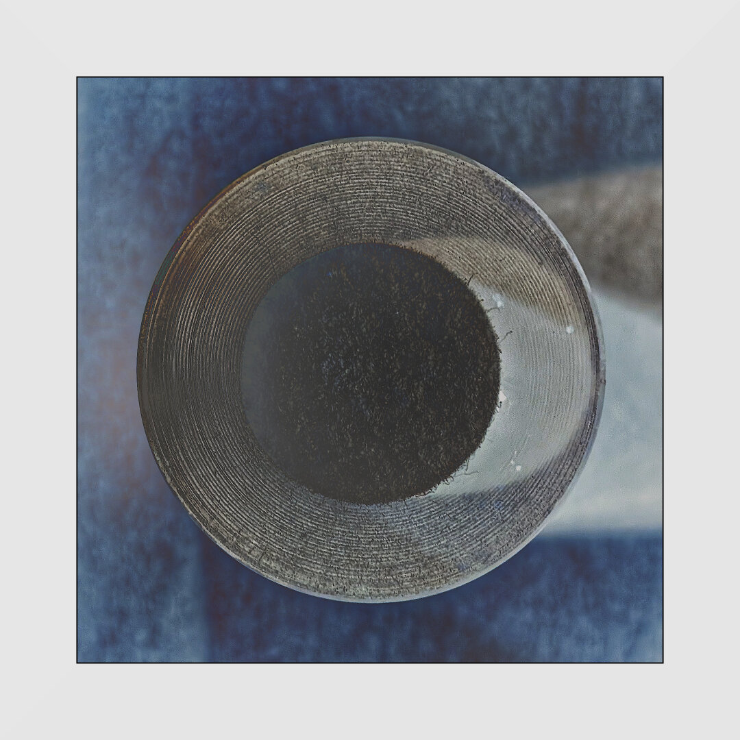 A basic circle in a square abstract composition in a heavily processed photograph an unrecognizable object. Dark blues and grays, some warm browns.