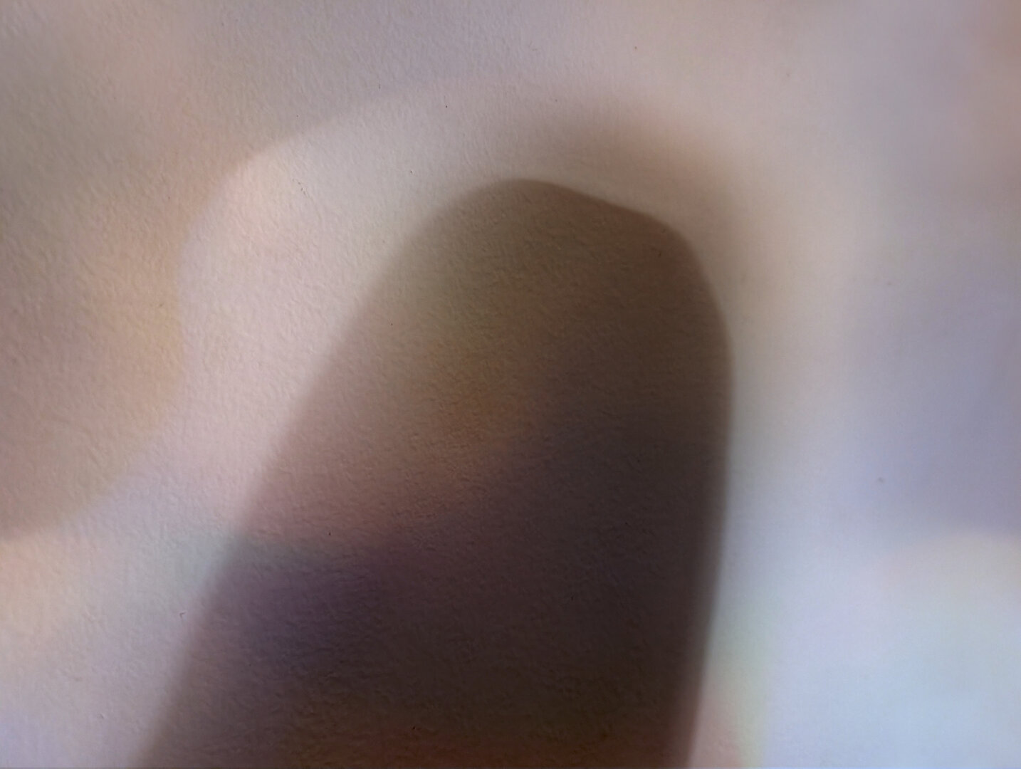 An upright knee and thigh cast a soft fuzzy shadow on the nearby wall. Only the shadow is visible.