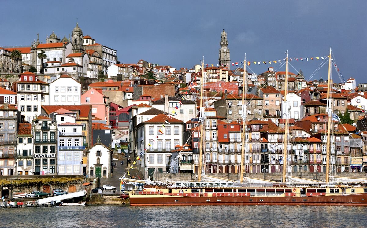 Vista da Ribeira, no Porto, com embarcação tradicional em primeiro plano e edifícios históricos alinhados na encosta.