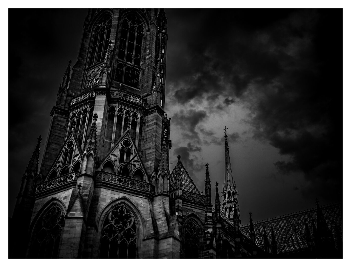 dramatic black-and-white photograph of a gothic cathedral
tall spires and pointed arches reaching toward a dark and cloudy sky
stonework, windows, and detailed carvings are accentuated by dim lighting and deep shadows
moody, atmospheric, threatening scene