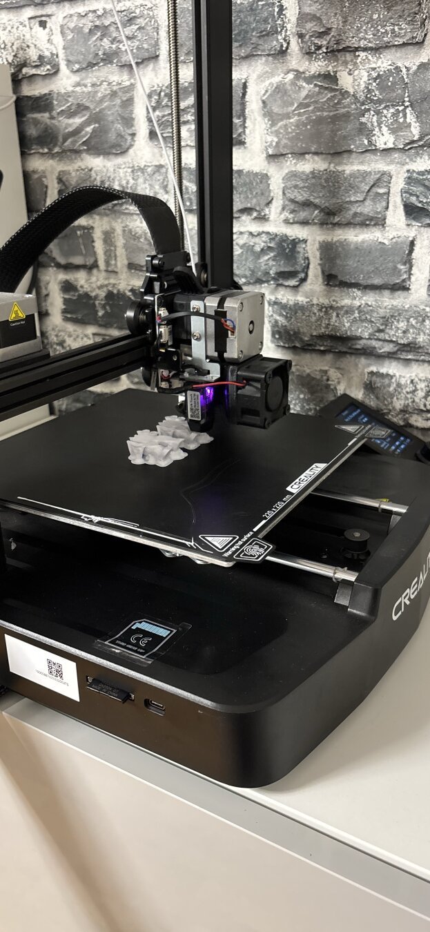 ein 3d drucker bei der arbeit. Auf der druckplatte sieht man die weißen Umrisse zweier Figuren