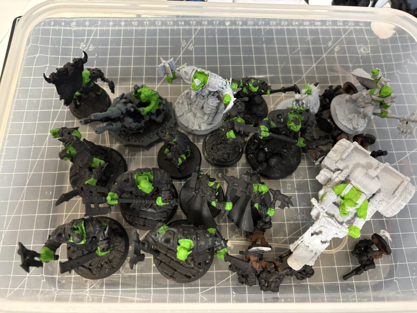 Eine Plastikbox mit schwarz grundierten Orks, die einen ersten grünen Anstrich belommen haben.