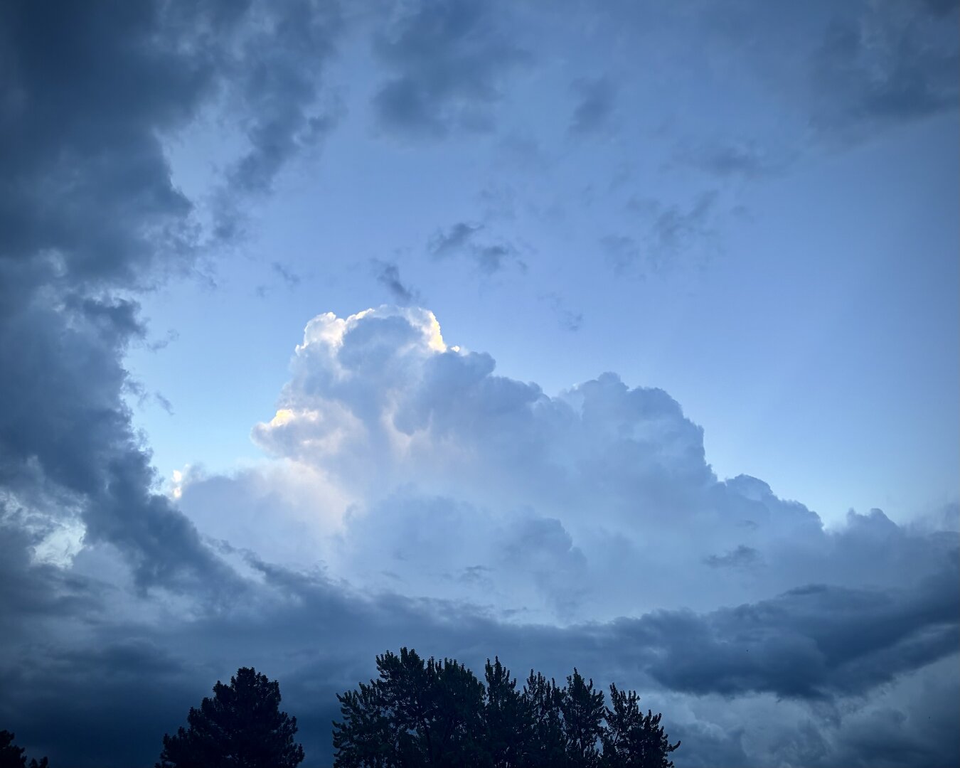 Ominous clouds surrounding a patch of clear sky. A large central cloud is backlit by the early morning sun.